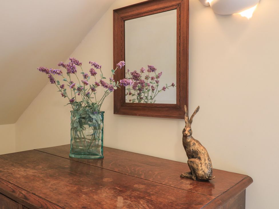 A wooden furniture with flowers in a vase and a rabbit statue at Bramble Cottage Babcary near Lydford-On-Fosse