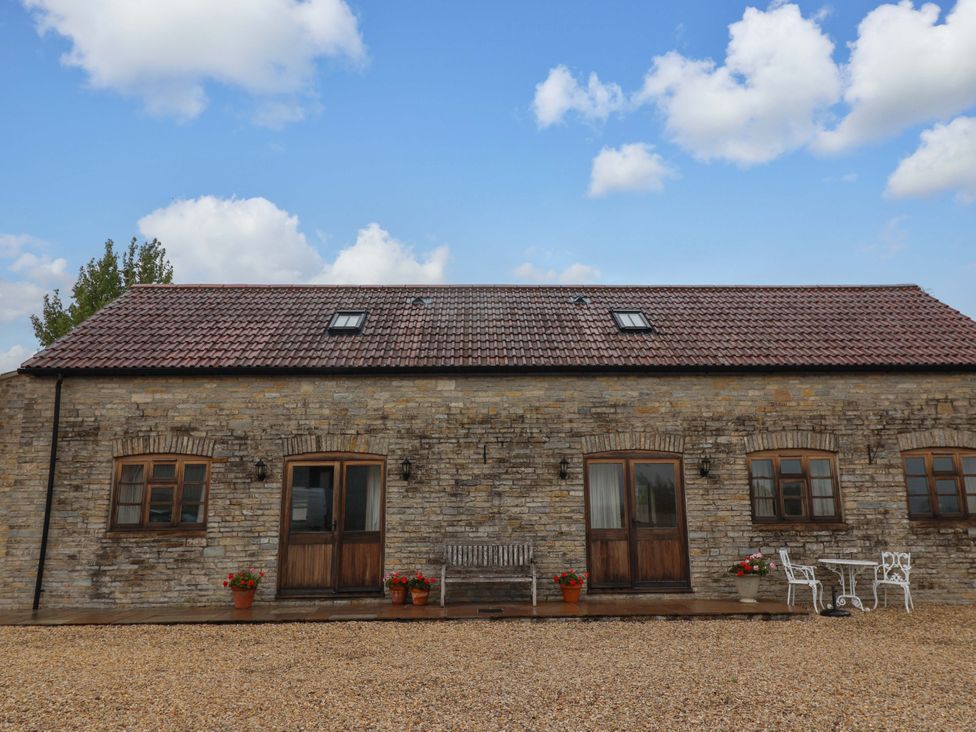 An exterior view of a stone house with a bench and flower pots at Badger Cottage in Lydford-On-Fosse
