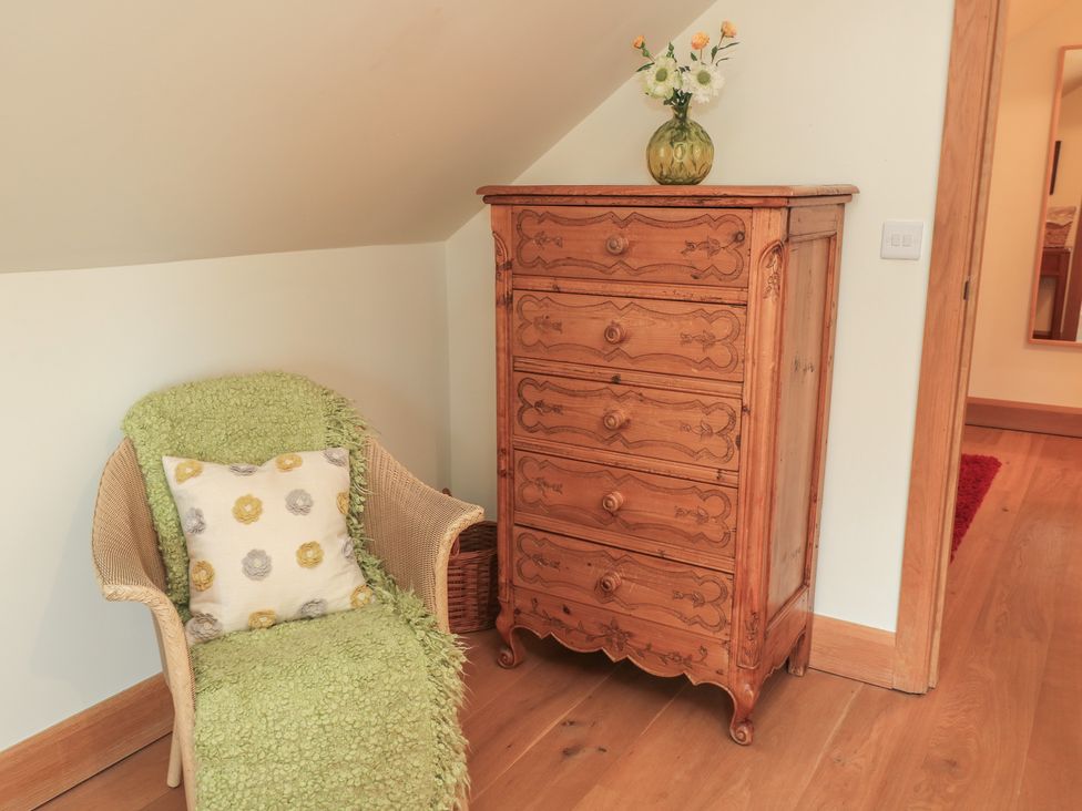 A chair with a blanket and cushion next to a chest of drawers at Badger Cottage Babcary near Lydford-On-Fosse