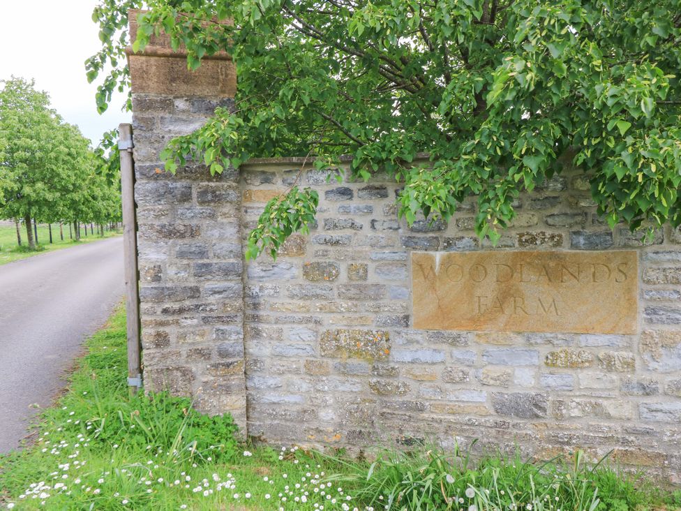 A stone wall with a sign at Woodlands Farm near a road with trees