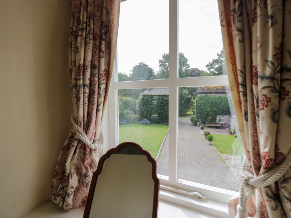 A view of a garden through a window with curtains at Longlands Milkmaid's Parlour in Cartmel near Grange-over-Sands