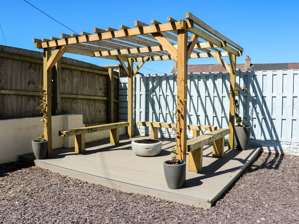 A pergola with benches and a fire pit in a garden at Rhiwlas Rhosneigr