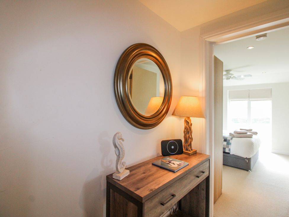 A bedroom with a wooden console table, lamp, and mirror at 7 Ocean's Edge in Thurlestone