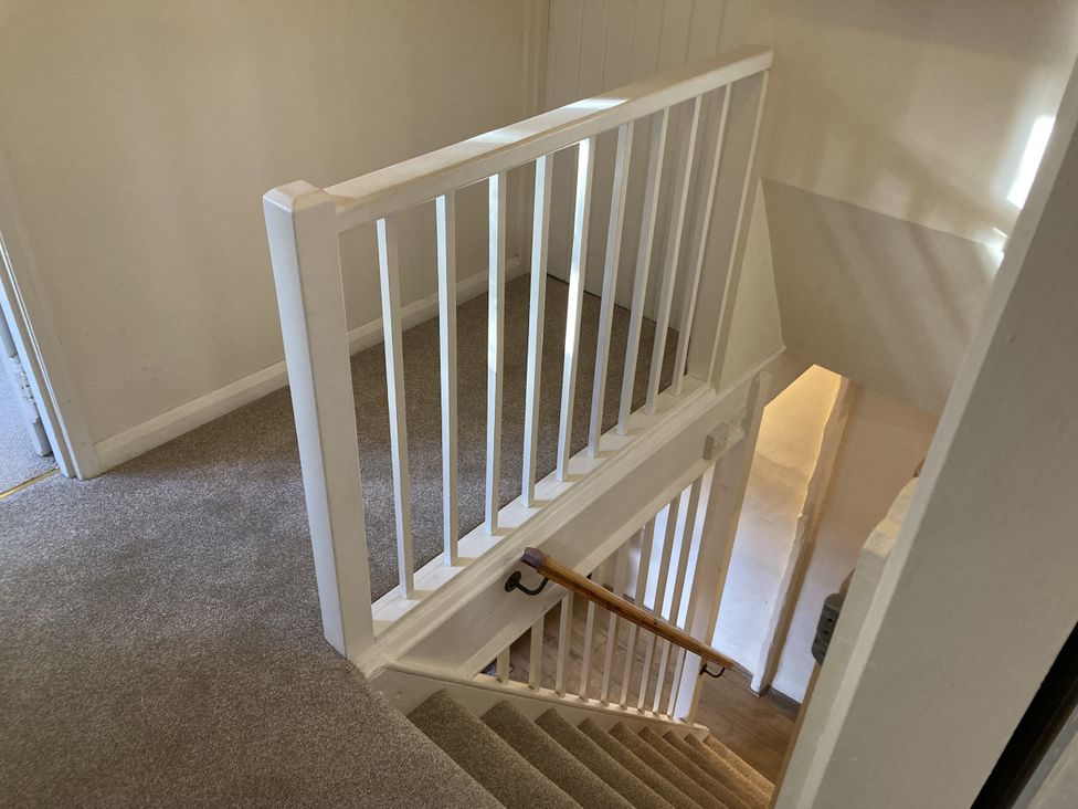 A hallway with a staircase and railing at Yew Tree Cottage in Stoke Fleming