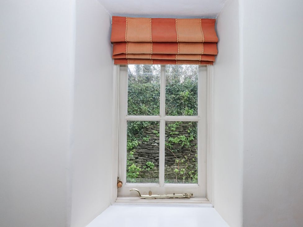 A window with a view of a stone wall and plants at Yew Tree Cottage in Stoke Fleming