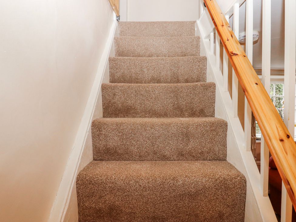 A staircase with carpeting and a wooden handrail at Yew Tree Cottage in Stoke Fleming