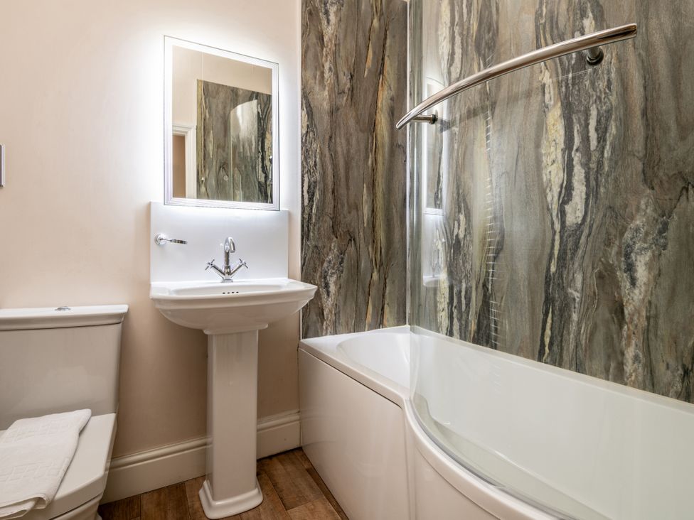 A bathroom featuring a toilet, sink, mirror, and bathtub at The Downwood in Blandford Forum