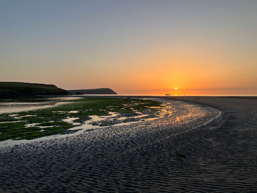 A beach at sunset with a boat on the water at West End Cottage, Newport, Pembrokeshire
