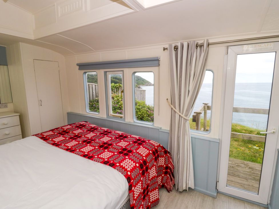 A bedroom with a bed and windows overlooking the sea at Clifftop Carriage in Aberporth, Ceredigion