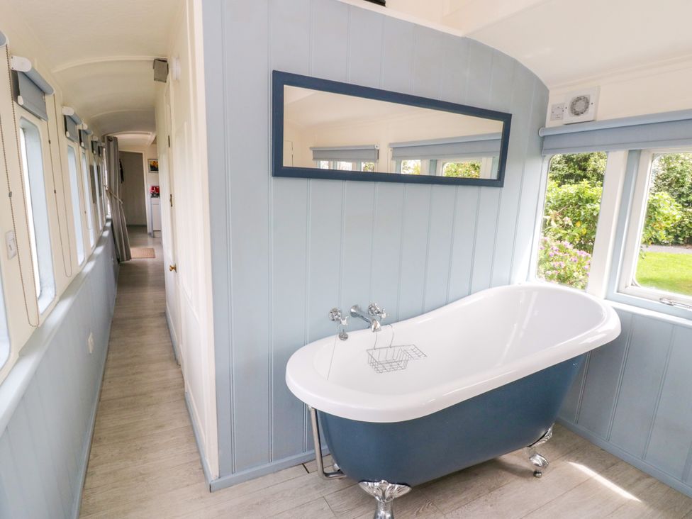 A bathtub with a mirror in the bathroom at Clifftop Carriage, Aberporth, Ceredigion