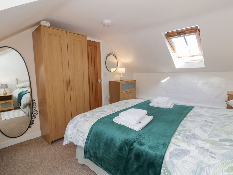 A bedroom with a bed, wardrobe, and mirror at End Cottage in Newport, Pembrokeshire