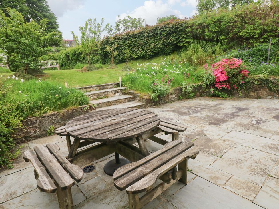 A garden with a stone patio and wooden table with benches at Brynawelon Newport, Pembrokeshire