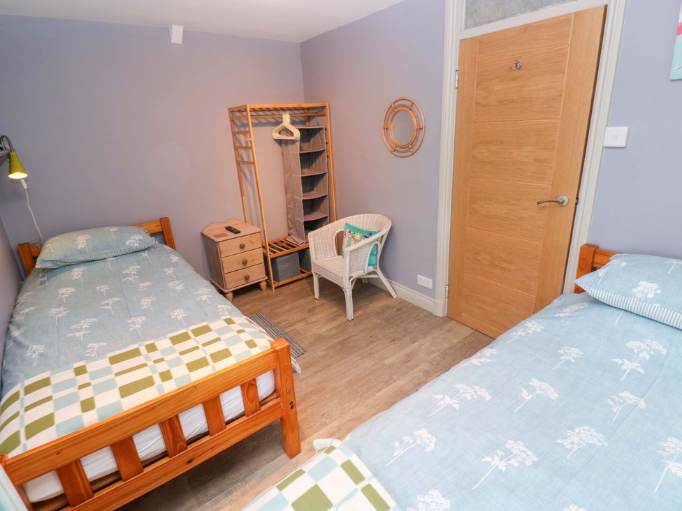 A bedroom with two beds, a chair, wardrobe, and door at Greenbanks in Dinas Cross, Pembrokeshire