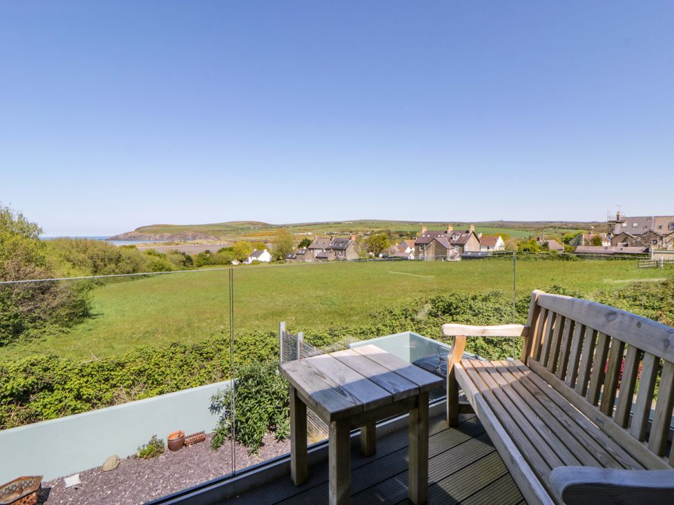 An outdoor area with a bench and table overlooking a field and houses at The Willows in Newport, Pembrokeshire