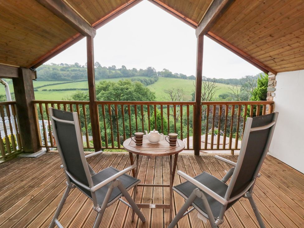 A balcony with chairs and a table overlooking hills at Dan Castell Cottage in Llandeilo, Carmarthenshire
