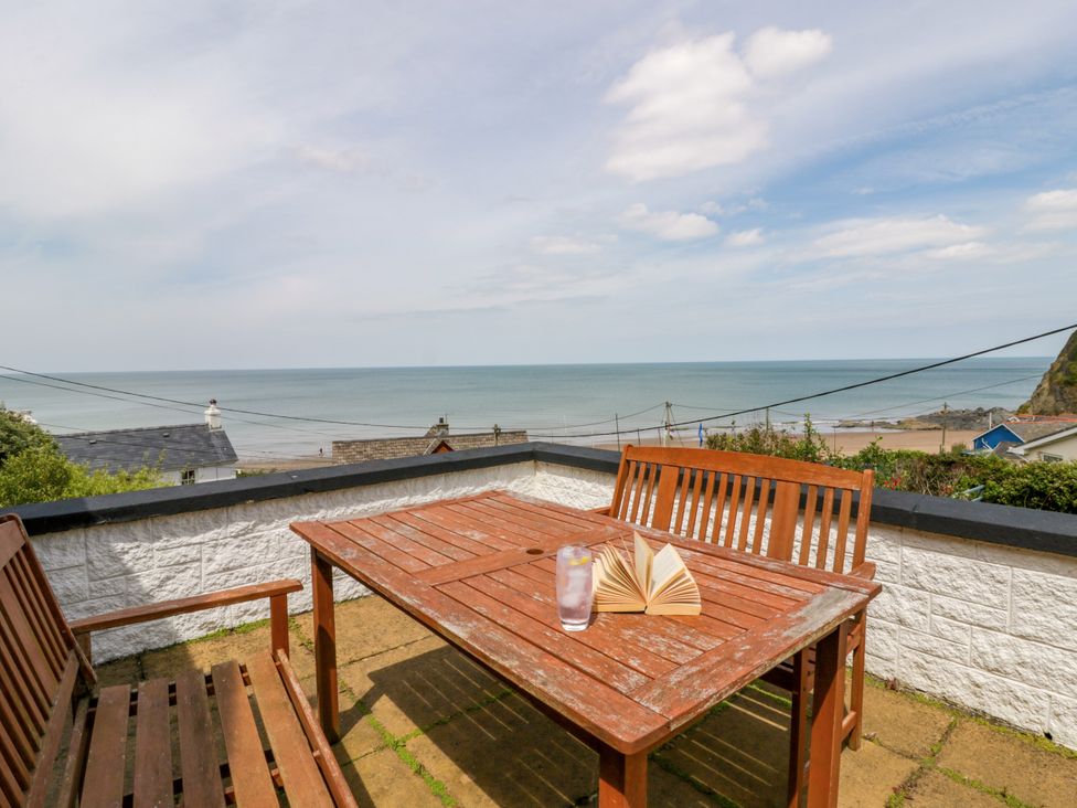 An outdoor seating area with a table, chairs, book, and glass overlooking the sea at Delyn Aur, Tresaith, Ceredigion