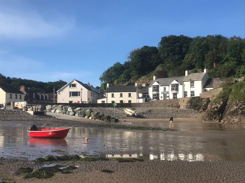 A beach scene with a red boat and houses at Beach Cottage in Little Haven, Pembrokeshire
