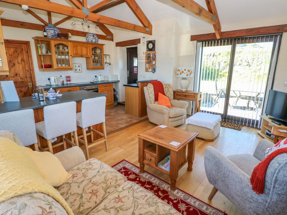 A living area with wooden beams a kitchen counter with bar stools armchairs a coffee table and sliding glass doors at Casa Mia in Strumble Head Goodwick