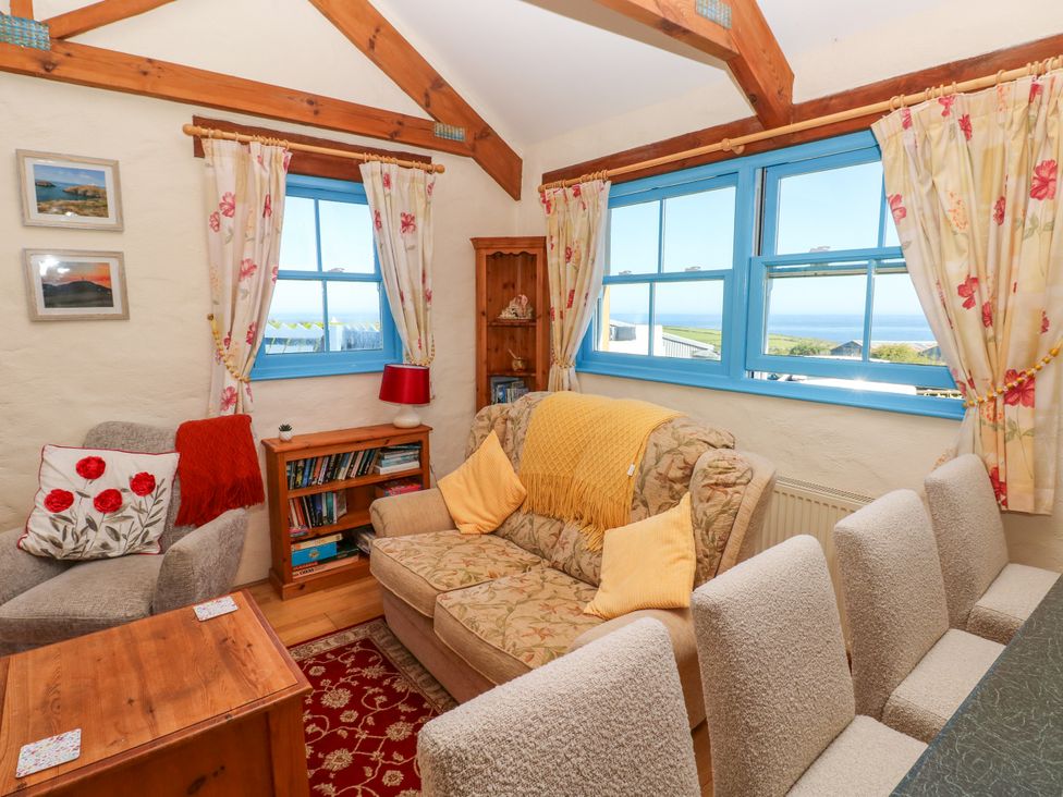 A living room with a floral sofa and armchair near blue windows with floral curtains at Casa Mia in Strumble Head Goodwick