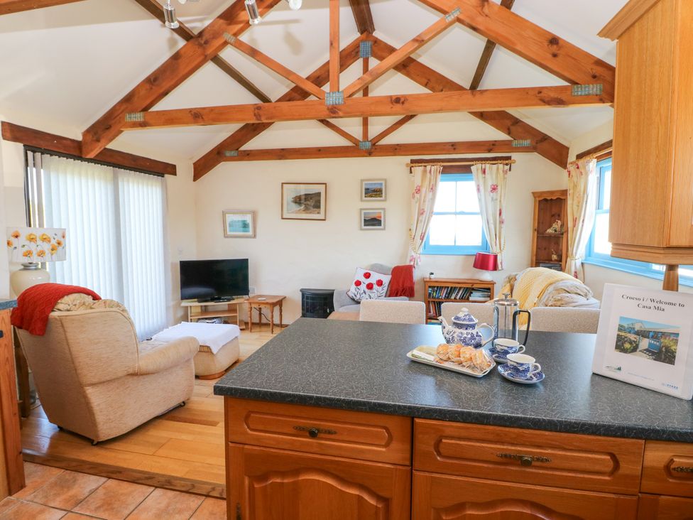 A living area with exposed wooden beams on the ceiling a TV armchairs an ottoman and a kitchen counter with tea set and a welcome sign at Casa Mia Strumble Head Goodwick