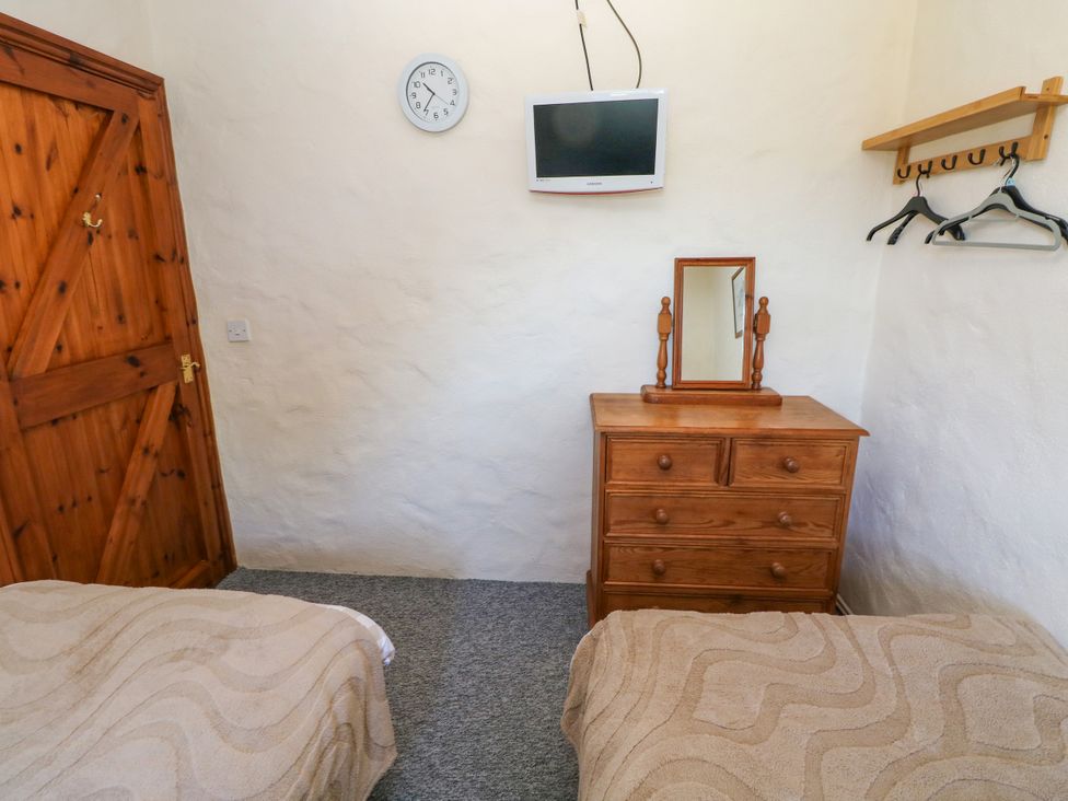 A bedroom with two single beds a wooden dresser and mirror a wall-mounted tv a clock and a wooden door at Casa Mia in Strumble Head Goodwick