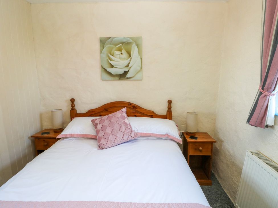 A bedroom with a wooden bed and two bedside tables with lamps and a painting of a white flower on the wall at Casa Mia in Strumble Head Goodwick