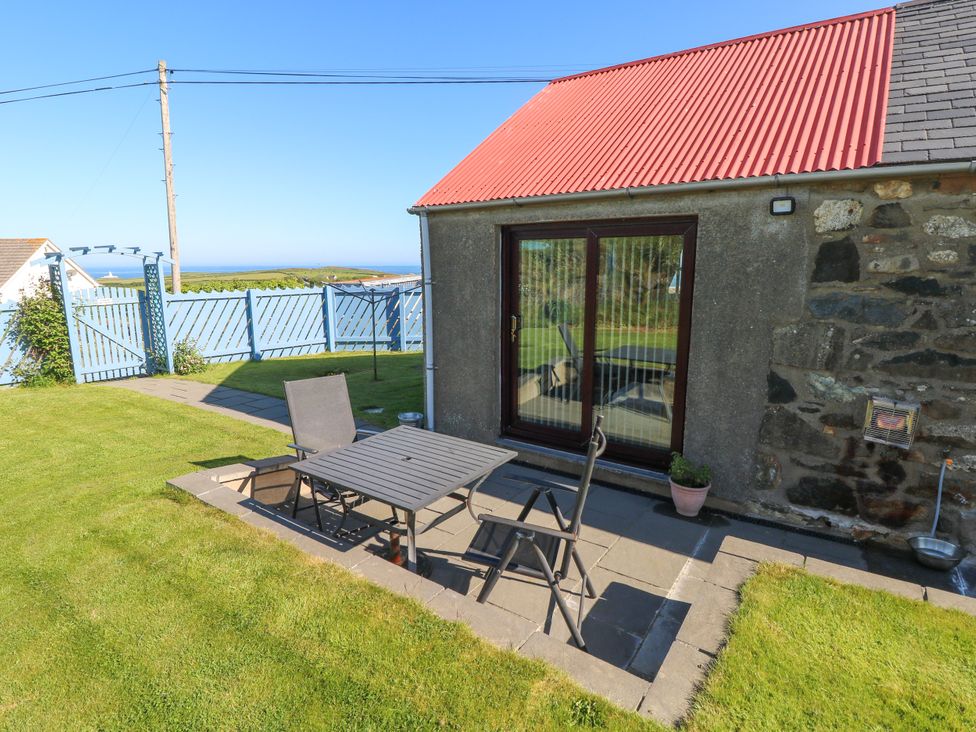 An outdoor patio with a table and two chairs next to a building with a red roof and stone wall at Casa Mia in Strumble Head Goodwick