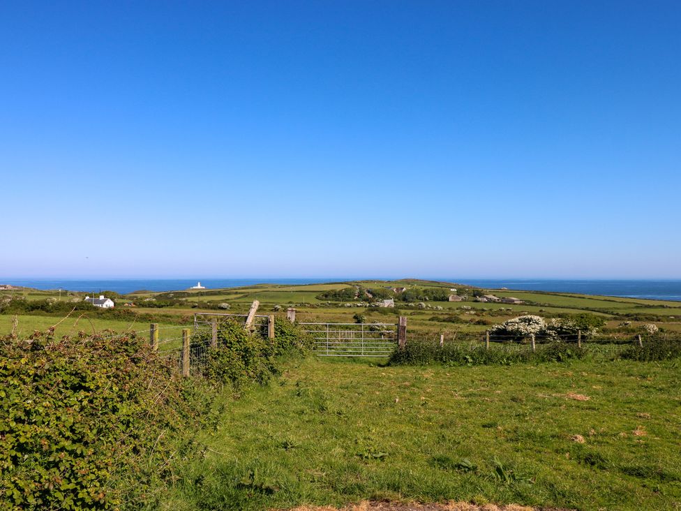 Green fields with a gate and fencing overlooking a coastal landscape with buildings and the sea at Casa Mia in Strumble Head Goodwick