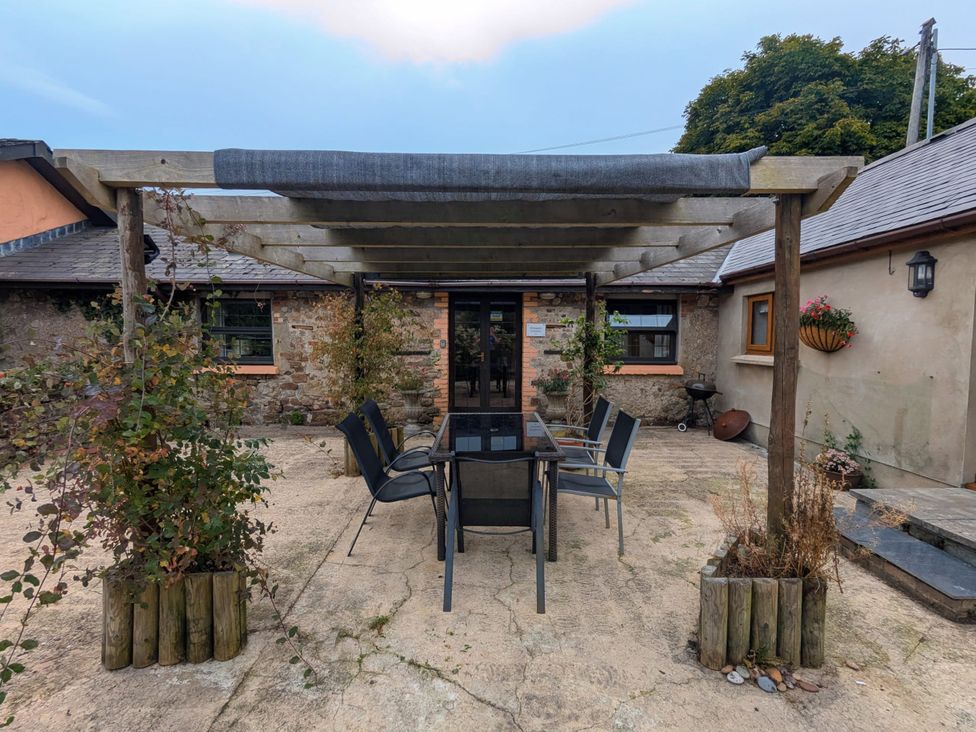 A dining area with a table and chairs under a pergola at Stoney Cottage in Narberth, Pembrokeshire