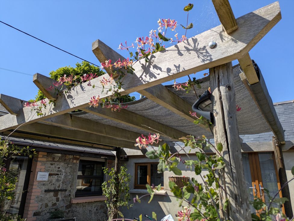 A pergola with flowers and a building at Stoney Cottage in Narberth, Pembrokeshire