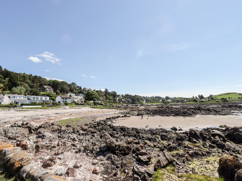 A beach with rocks and houses in the background at The Barn in Rockcliffe