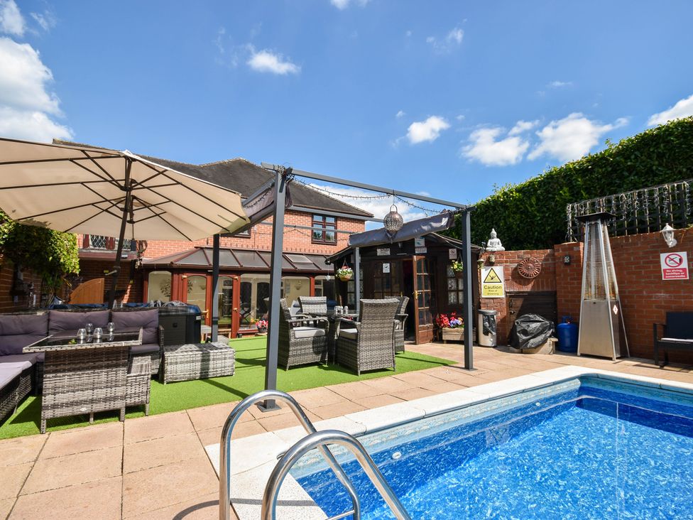 A garden with a swimming pool and seating area at Freshwinds in Market Drayton