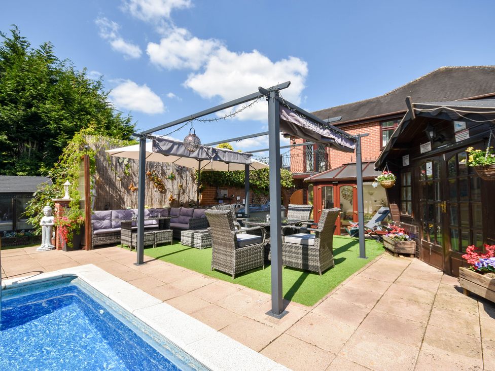 A garden with a swimming pool and seating area at Freshwinds in Market Drayton