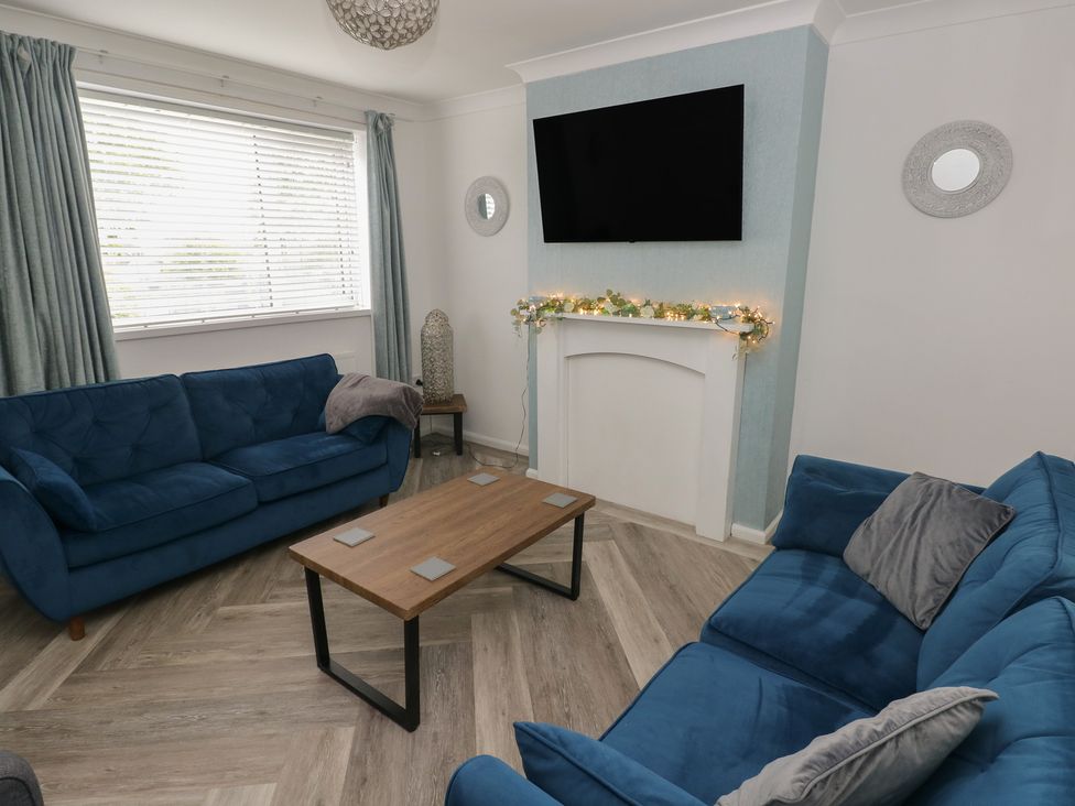 A living room with blue sofas and a coffee table at Cwtch Ar Y Mor in Burry Port