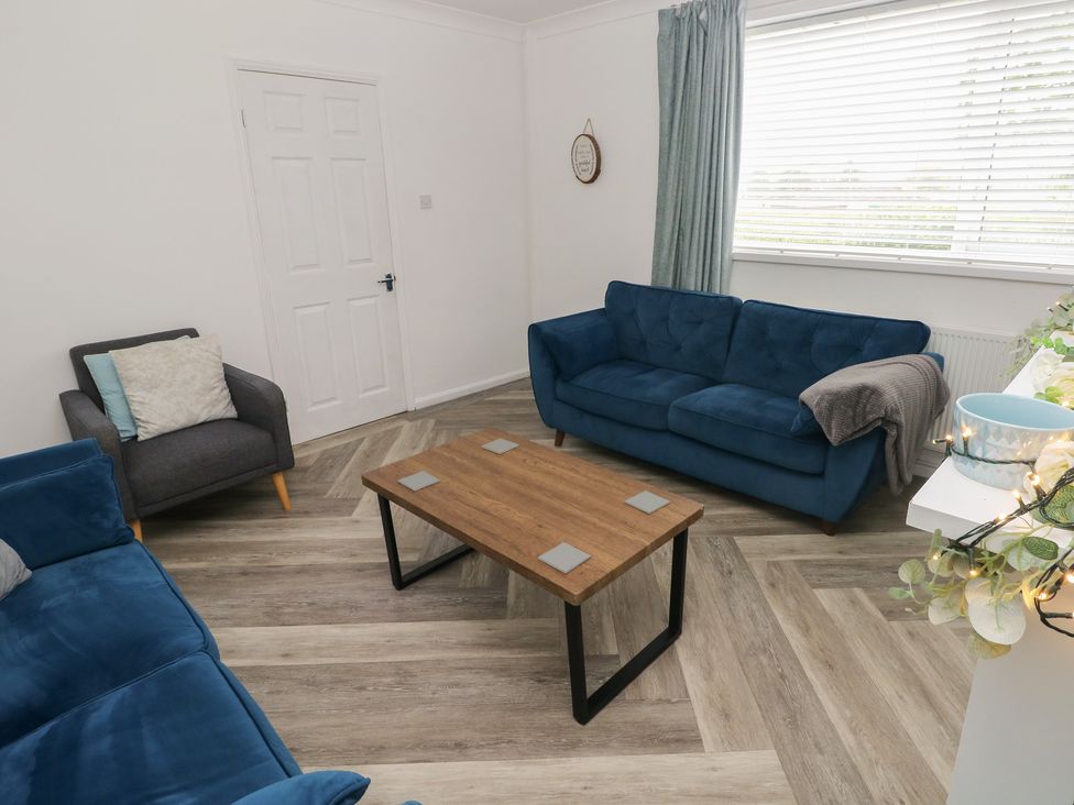 A living room with a blue sofa and armchair next to a coffee table at Cwtch Ar Y Mor in Burry Port