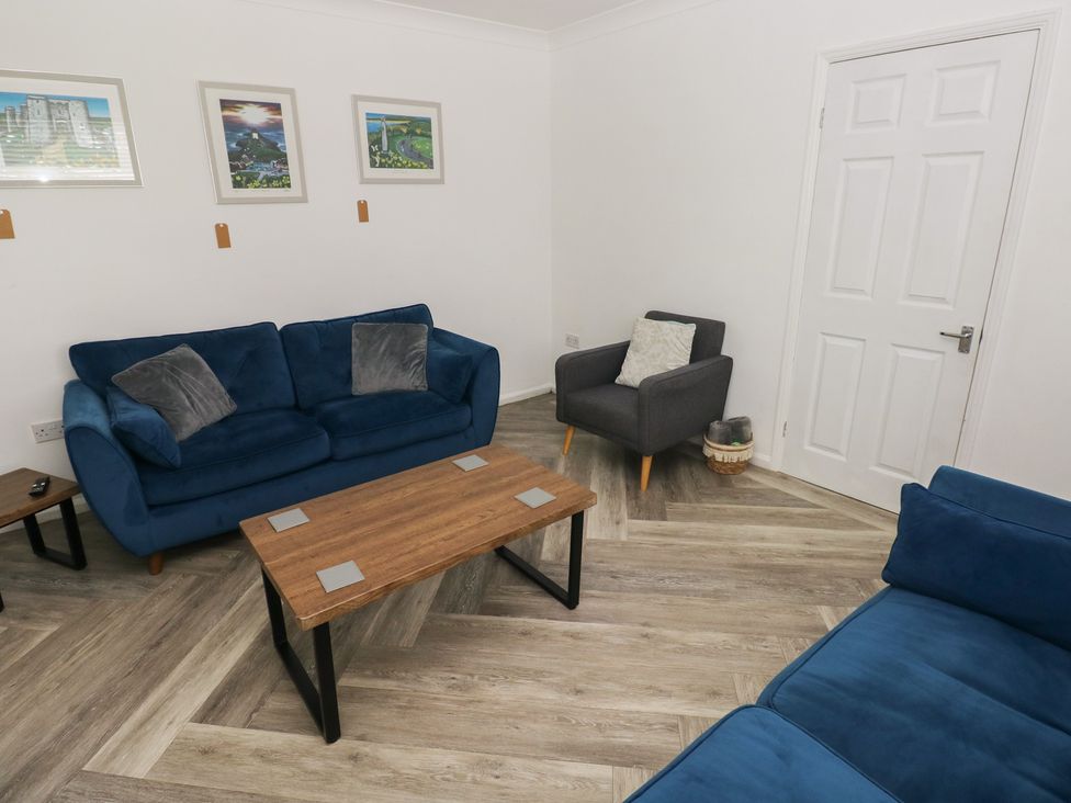 A living room with a blue sofa and wooden coffee table at Cwtch Ar Y Mor Burry Port