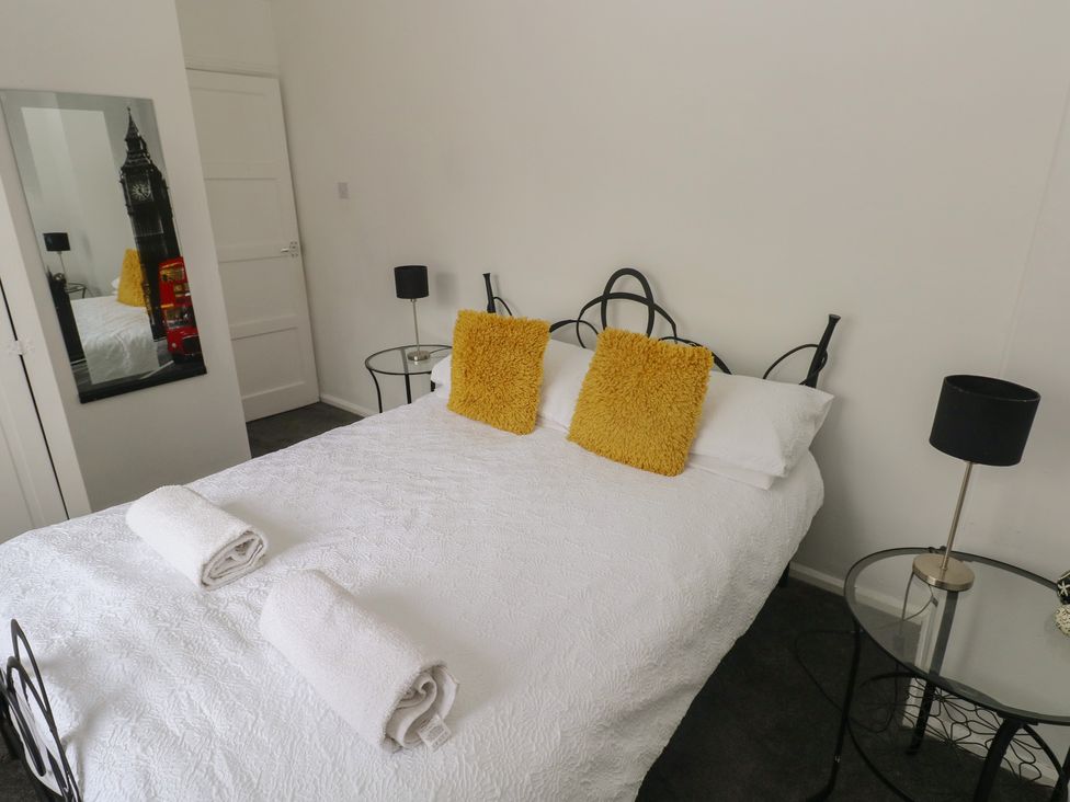 A bedroom with a bed, pillows, towels, mirror, and lamps at Cwtch Ar Y Mor in Burry Port