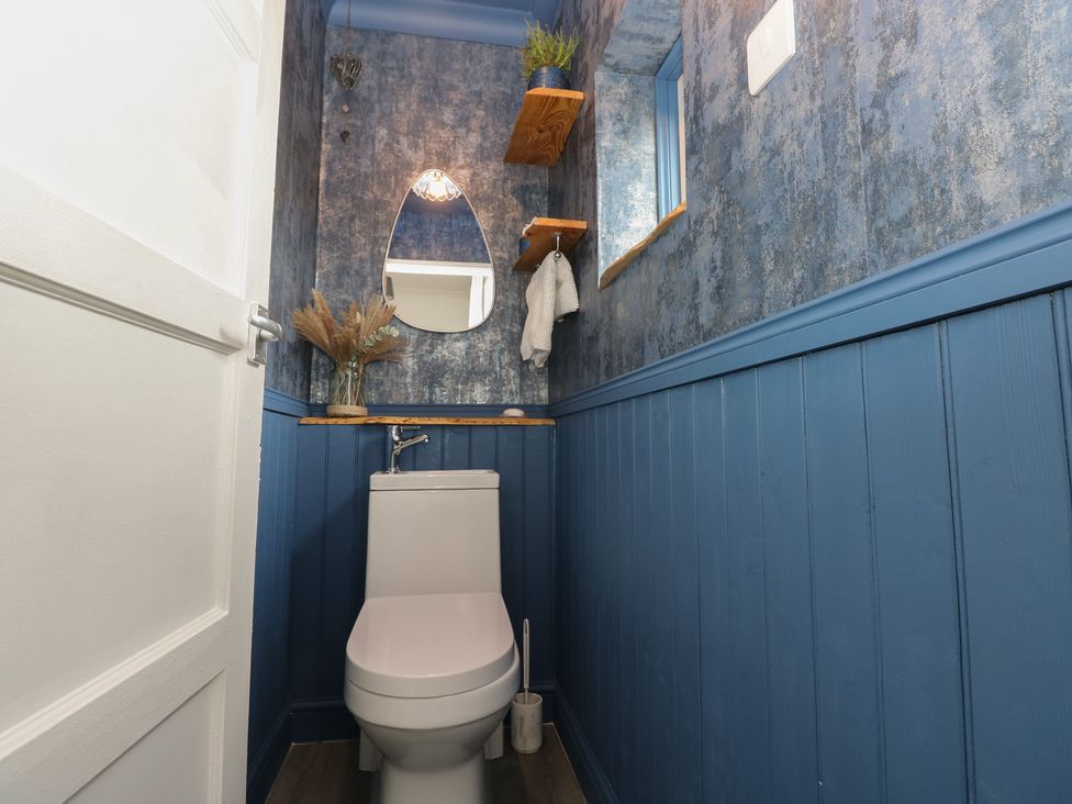 A bathroom with a toilet, mirror, and shelf at Cwtch Ar Y Mor in Burry Port