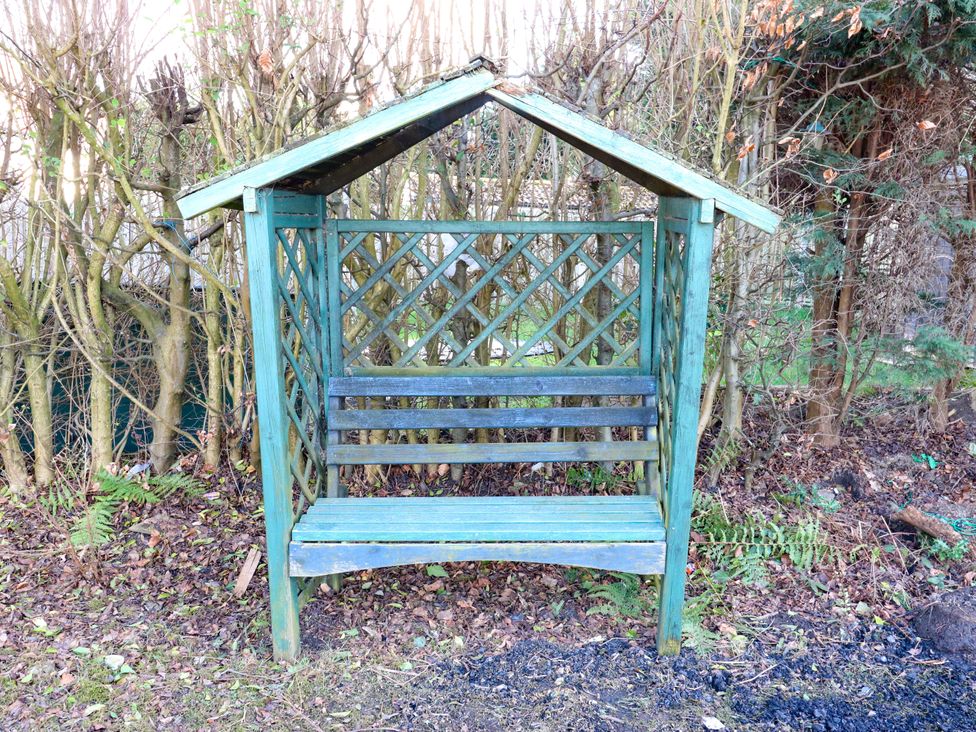 A wooden bench with a roof and lattice design in a garden at Hira's Cottage