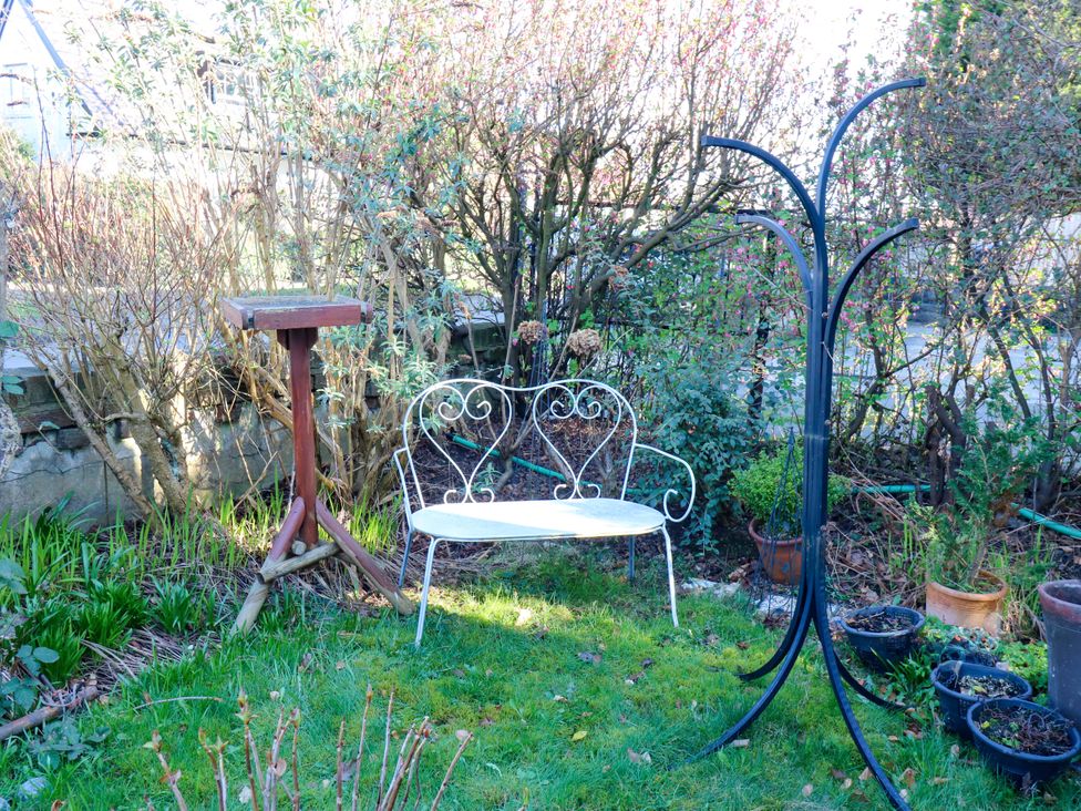 A garden with a bench and bird feeder at Hira's Cottage