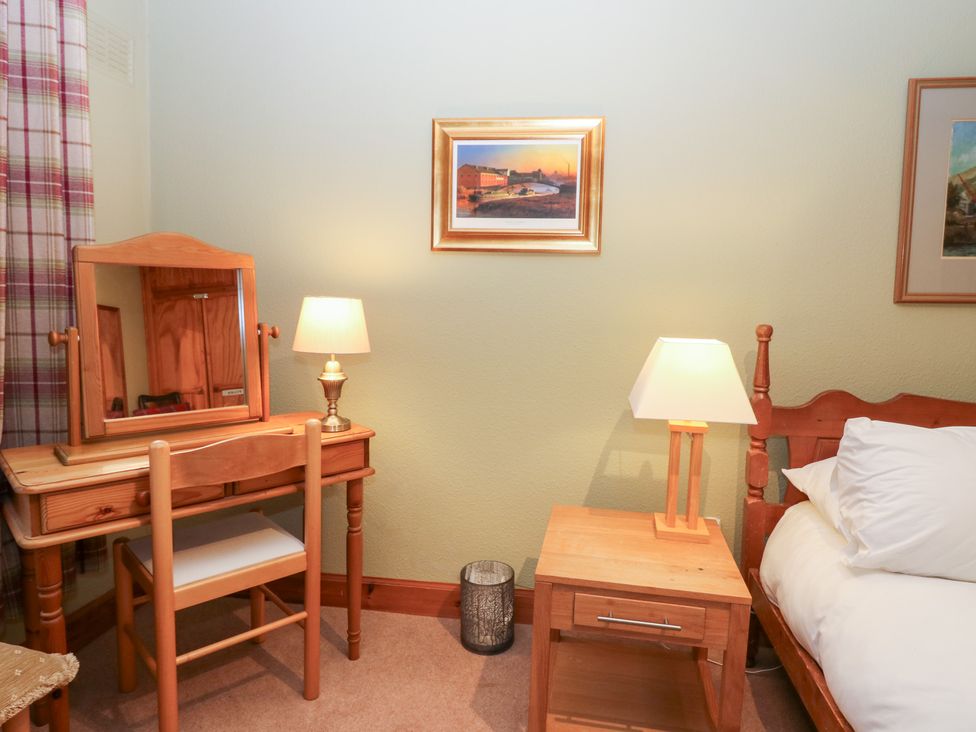 A bedroom with a mirror, lamp, chair, table, and bed at 1 The Cross in Dunkeld