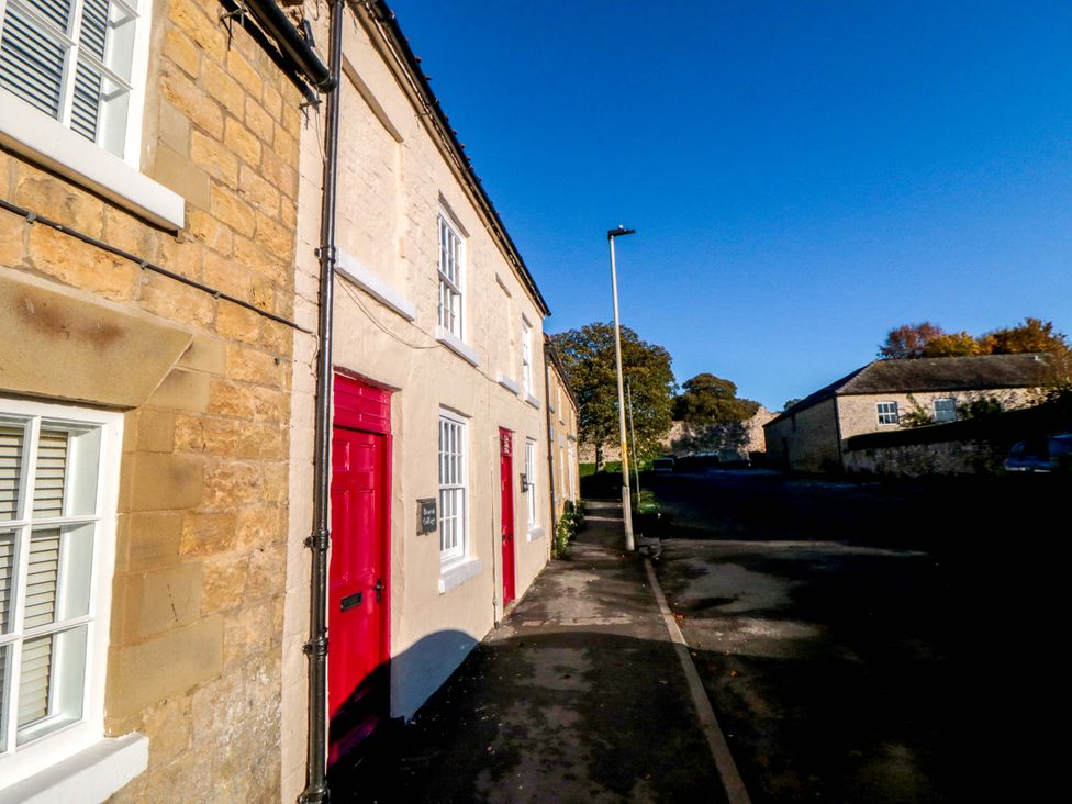 An outdoor view of a building with red doors and a stone wall at Beacon Cottage in Pickering