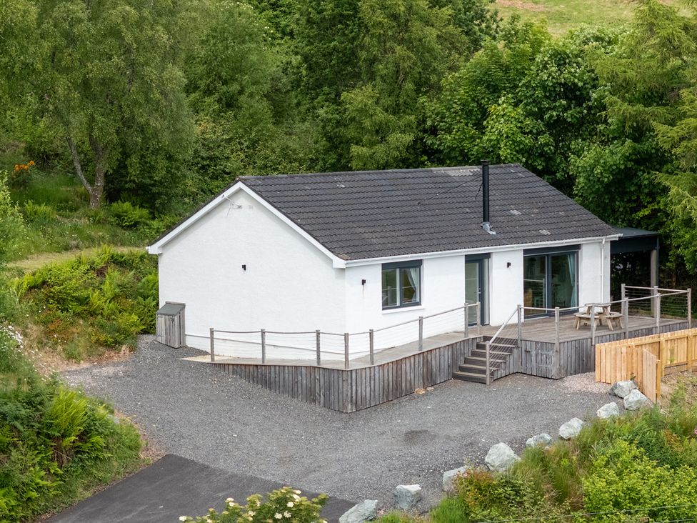 A white house with a tiled roof and wooden deck surrounded by trees at The Lookout in Saasaig near Broadford