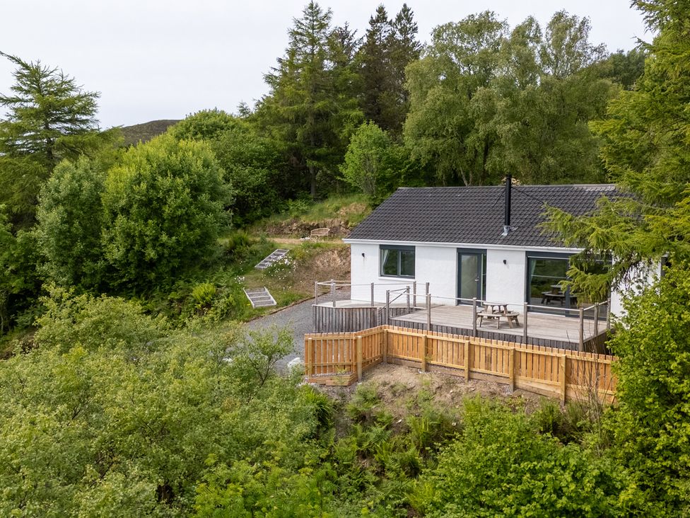 A white house with a grey roof surrounded by trees and a wooden fence at The Lookout in Saasaig near Broadford