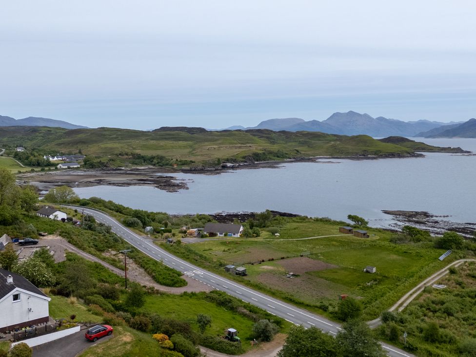 A coastal landscape with a winding road beside houses and green fields overlooking a body of water with hills and mountains in the background at The Lookout in Saasaig near Broadford