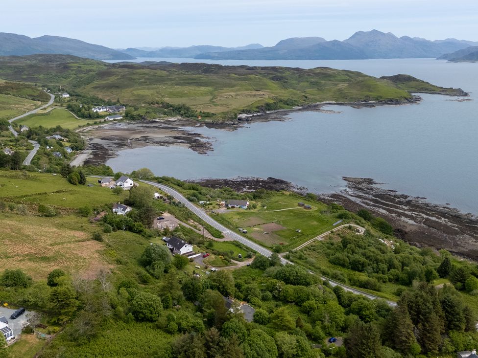 A coastal landscape with houses, a road, green hills, and mountains across the water at The Lookout in Saasaig near Broadford