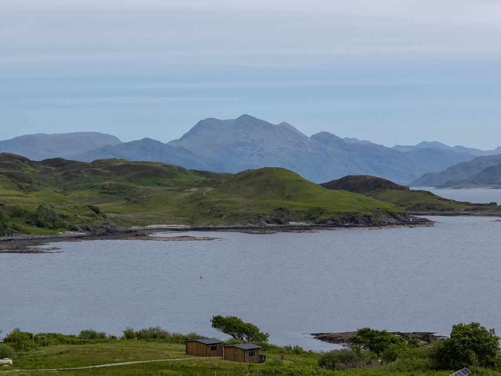 A coastal landscape with two wooden cabins on grassy land near a body of water and hills in the background at The Lookout in Saasaig near Broadford
