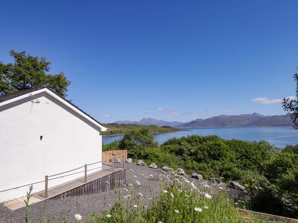 A house with a decking area overlooking a body of water and mountains at The Lookout in Saasaig near Broadford