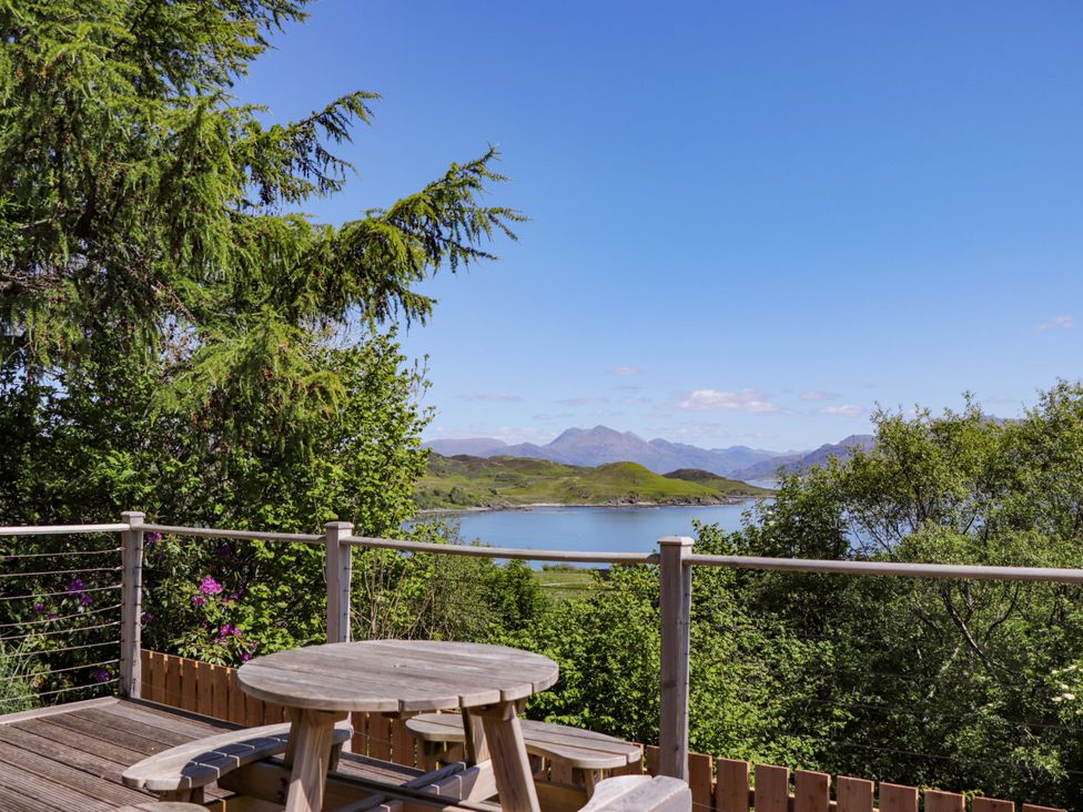 A deck with a table and chairs overlooking a lake at The Lookout in Saasaig near Broadford