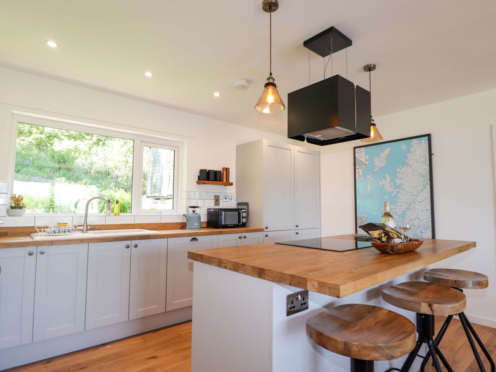 A kitchen with a sink, countertop, microwave, and stools at The Lookout in Saasaig near Broadford